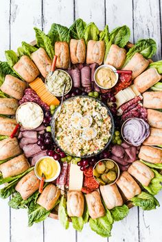 a platter filled with meats, vegetables and dips on a white wooden table