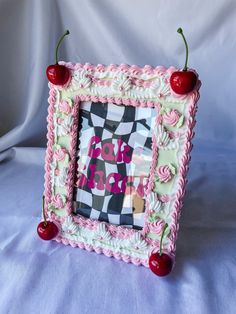 a pink and white photo frame with cherries on the top, sitting on a bed