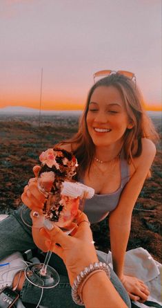 a woman sitting on top of a blanket holding an ice cream sundae