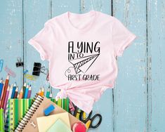 Get ready to soar into a new school year with our Flying Into First Grade Shirt! Perfect for your little one's first-grade adventures, this shirt is designed to celebrate this exciting milestone with style and fun. 🌟🎉 Comfortable Fabric: Made from soft, breathable material to keep your child comfy all day long. ☁️👕 Adorable Design: Features a cute airplane graphic with "Flying Into First Grade" text, making it a delightful choice for school days. ✈️❤️ Perfect Fit: Available in various sizes to ensure a great fit for your growing first-grader.  Versatile Wear: Ideal for the first day of school, picture day, or any school event. Pairs well with jeans, shorts, or skirts!  Great Gift: A wonderful gift for your child or any first-grader, making their new school year even more special. 🎁🎒 C Back To School Letter Print Tops For School Events, Text Print Tops For Back To School, Educational College T-shirt With Letter Print, Back To School Text Print Tops, Back To School Letter Print Tops, Back To School Slogan Tops For College, Slogan Tops For College And Back To School, Back To School Tops With Letter Print, Letter Print Tops For School Events At Year End