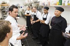 a group of people standing in a kitchen talking to each other and holding food items