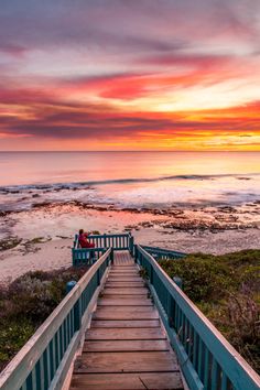 a person sitting on a bench at the end of a wooden walkway next to the ocean