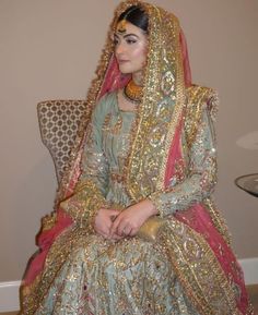 a woman sitting in a chair wearing a gold and green dress with an elaborate head piece