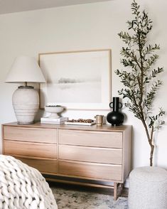 a white vase sitting on top of a wooden dresser next to a tree in a living room