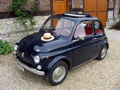 an old blue car with a hat on the hood parked in front of a brick building