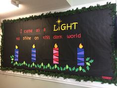 a bulletin board with candles and holly garland on the bottom, saying light to shine on this dark world