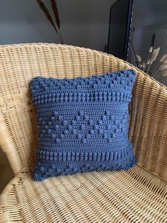 a blue crocheted pillow sitting on top of a wicker chair next to a plant