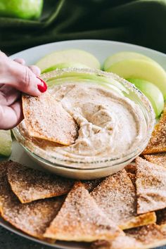 a person dipping an apple into a bowl of dip surrounded by tortilla chips