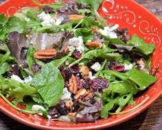 a red bowl filled with green salad and nuts