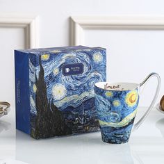 a coffee cup sitting on top of a table next to a box with the painting van gogh