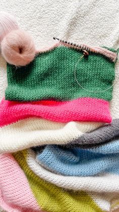 a pile of different colored knitted items on top of each other, including a ball of thread