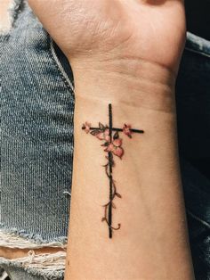 a woman's wrist with a cross and flowers tattoo on her left side arm