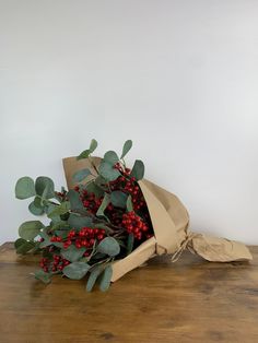 a bouquet of red berries and greenery wrapped in brown paper on a wooden table