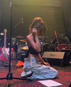 a woman sitting on the floor while talking on her cell phone and holding a guitar