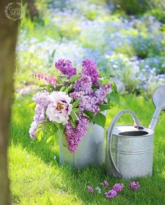 a watering can with flowers in it sitting on the grass