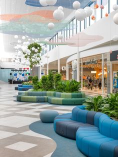 the interior of a shopping mall with blue and green seats, plants and lights hanging from the ceiling