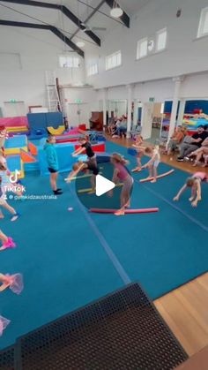 a group of children are practicing gymnastics in an indoor gym with blue flooring and walls