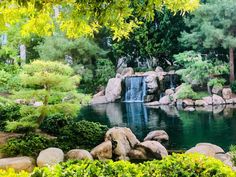 a pond surrounded by rocks and trees with a waterfall in the middle is surrounded by greenery