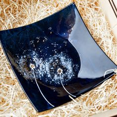 a blue glass dish with white flowers on it in a box filled with straws