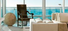 a living room filled with white furniture and large windows overlooking the ocean on a sunny day