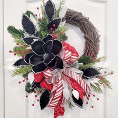 a christmas wreath with black and red flowers on the front door, decorated with candy canes