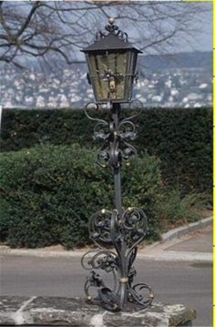 an old fashioned street light on the side of a road with trees in the background