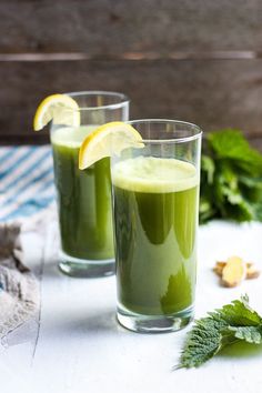 two glasses filled with green smoothie next to mint and lemon wedges on a table