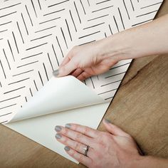 a woman is wrapping up a piece of white paper on top of a wooden table