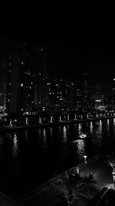 black and white photograph of city lights along the riverbank at night with buildings in the background