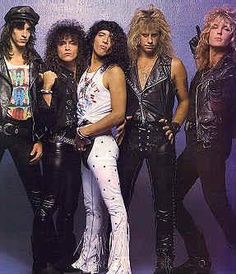 the band kiss posing for a photo in their leather outfits, with one arm around the other's shoulder