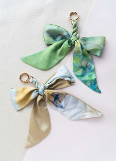 three pieces of fabric tied together with gold metal scissors on a white surface, one has a green bow and the other two are different colors