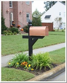 a mailbox sitting in the middle of a flower bed next to a sidewalk and house