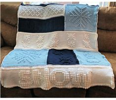 a blue and white crocheted blanket sitting on top of a couch next to a pillow