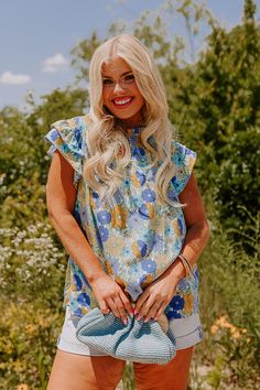 - Embrace feminine florals this season with this sweet top! - Unlined material with a colorful floral print - A ruffled v-notched neckline - A smocked upper bodice - Short flutter sleeves - A relaxed silhouette that ends in a rounded hemline Blue Floral Print Tops With Ruffle Sleeves, Blue Ruffle Sleeve Tops For Vacation, Blue Bohemian Blouse With Ruffle Sleeves, Bohemian Blue Blouse With Ruffle Sleeves, Floral Print Ruffle Sleeve Blouse For Vacation, Vacation Blouse With Floral Print And Flutter Sleeves, Blue Flutter Sleeve Tops With Floral Print, Blue Floral Print Top With Flutter Sleeves, Blue Flutter Sleeve Blouse For Vacation