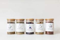 four jars filled with different types of spices on a white surface, each containing an individual's own name