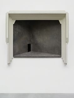 an open window in the side of a white wall with columns on either side and a black square opening at the end