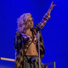 a woman standing in front of a microphone on stage with her hand up to the side