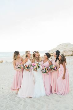 the bride and her bridesmaids pose for a photo on the beach in pink dresses