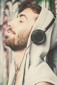 a man with headphones resting against a wall covered in graffiti, listening to music