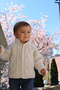 a little boy standing next to a tree with pink flowers