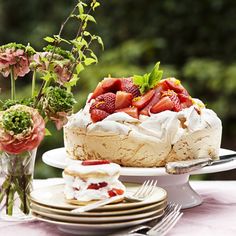 a cake with strawberries on top is sitting on a table next to plates and flowers