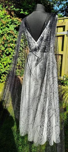 a black and white dress on display in front of a wooden fence with bushes behind it