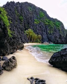 the beach is surrounded by large rocks and palm trees