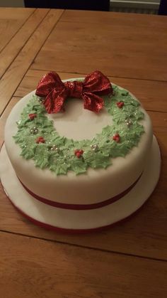 a white cake decorated with holly wreaths and red bows on top of a wooden table