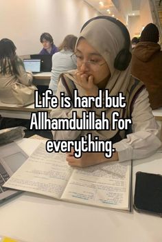 a woman sitting at a desk with headphones on and looking at an open book