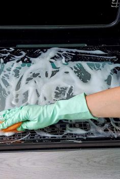 a person in green gloves is cleaning an oven with foam on the bottom and inside