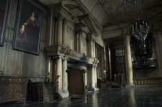 an empty room with columns and paintings on the wall, in front of a chandelier