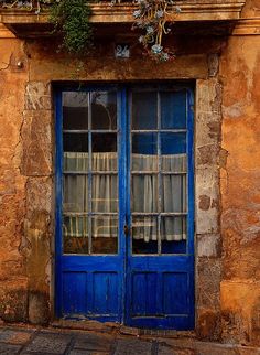 an old building with two blue doors and window frames on the outside, in front of it