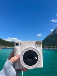 a person holding up a camera in front of the water