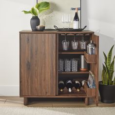 a wooden cabinet filled with bottles and glasses next to a potted plant on top of a rug